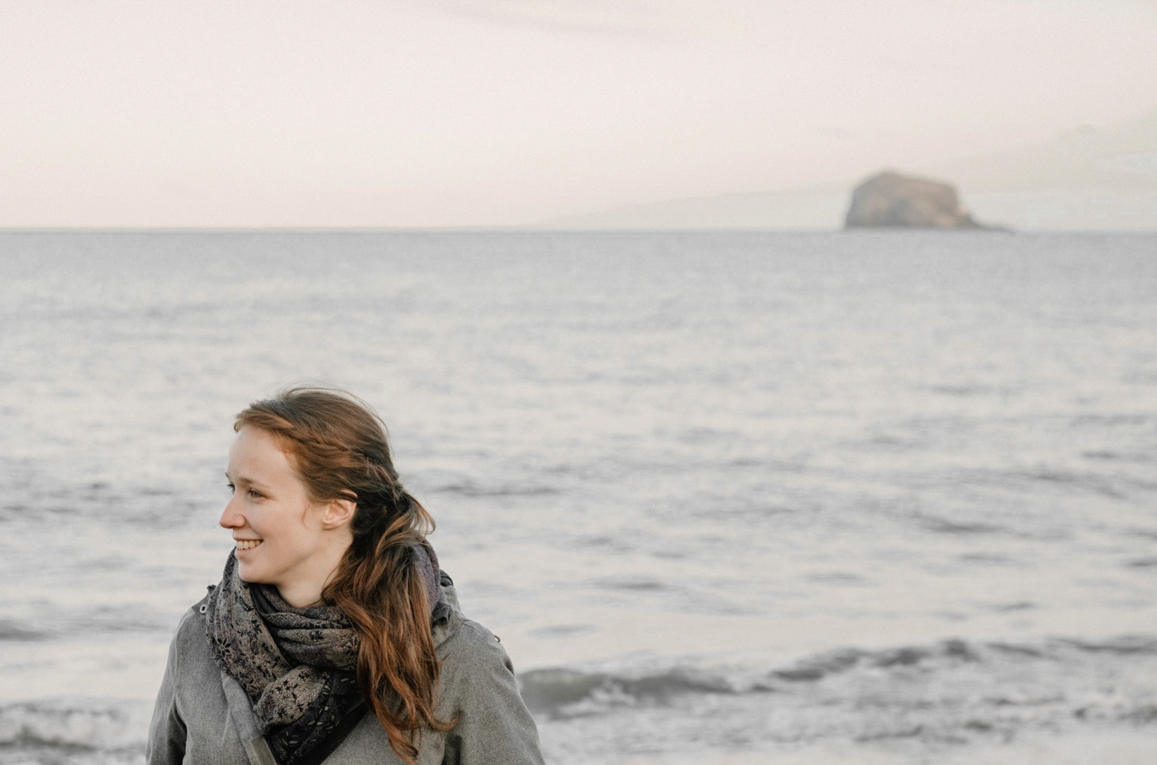Woman standing on a beach with the Bass Rock formation in the distance