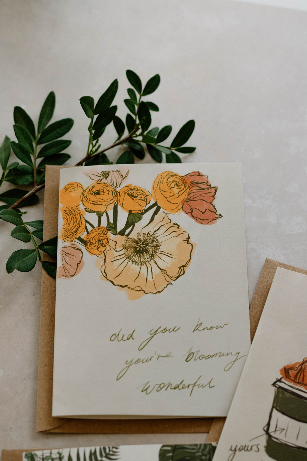 A6 card with floral illustration on top of a Kraft brown envelope with fresh foliage in the top left corner