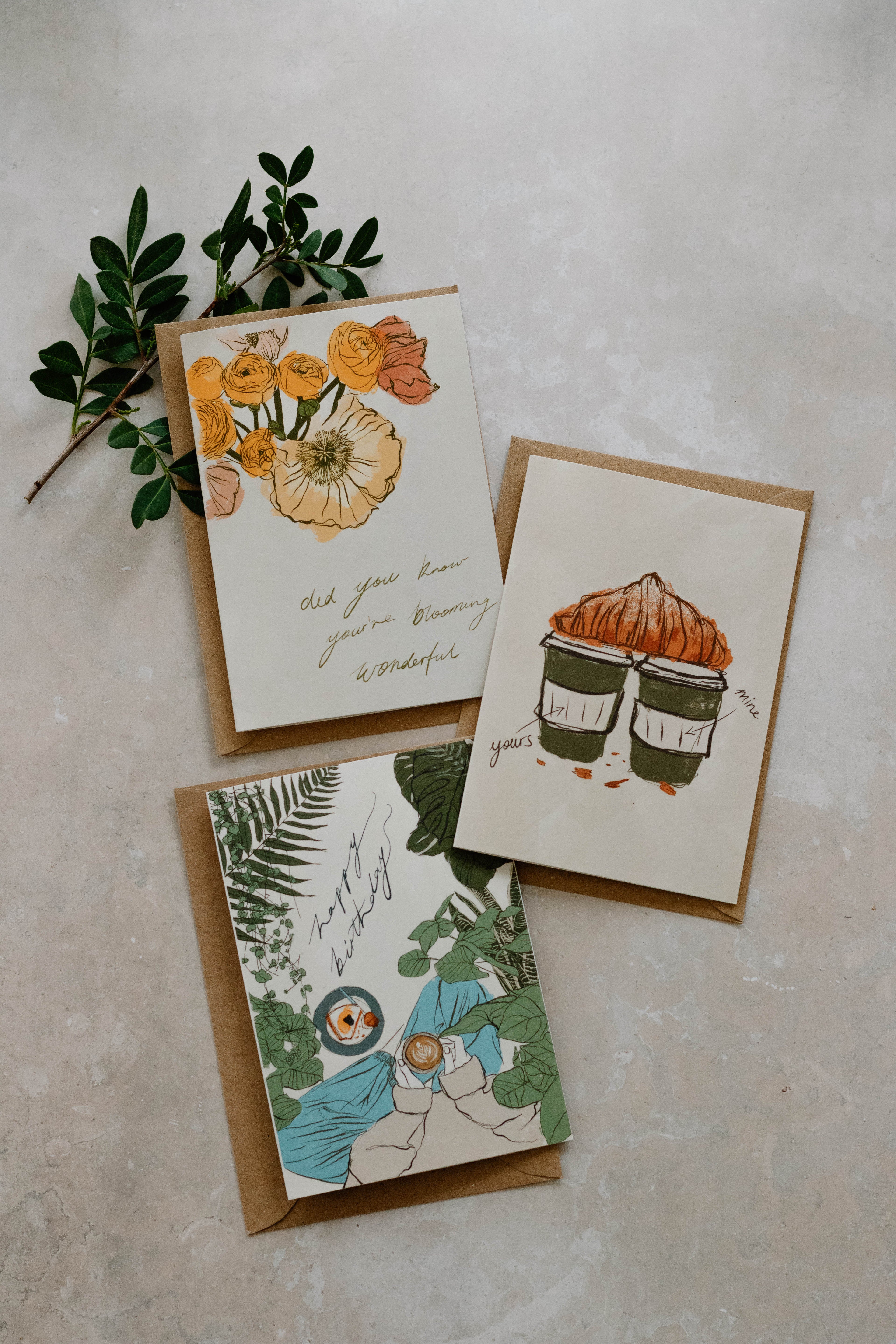 3 A6 greeting cards with botanical and floral illustrations. Each one placed on a Kraft brown envelope. Fresh foliage borders the top left corner.