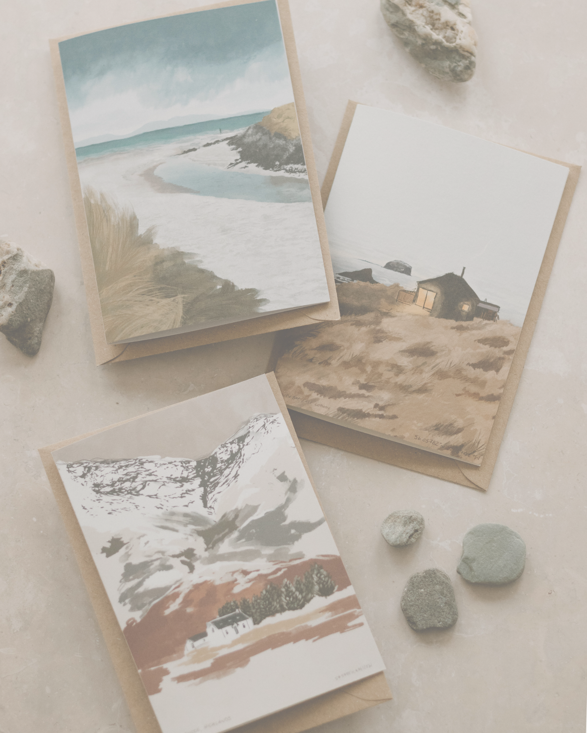 Three scenic greeting cards on a textured surface with stones.