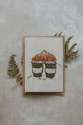 Card with illustration of two coffee cups and a pastry on a textured surface with leaves.