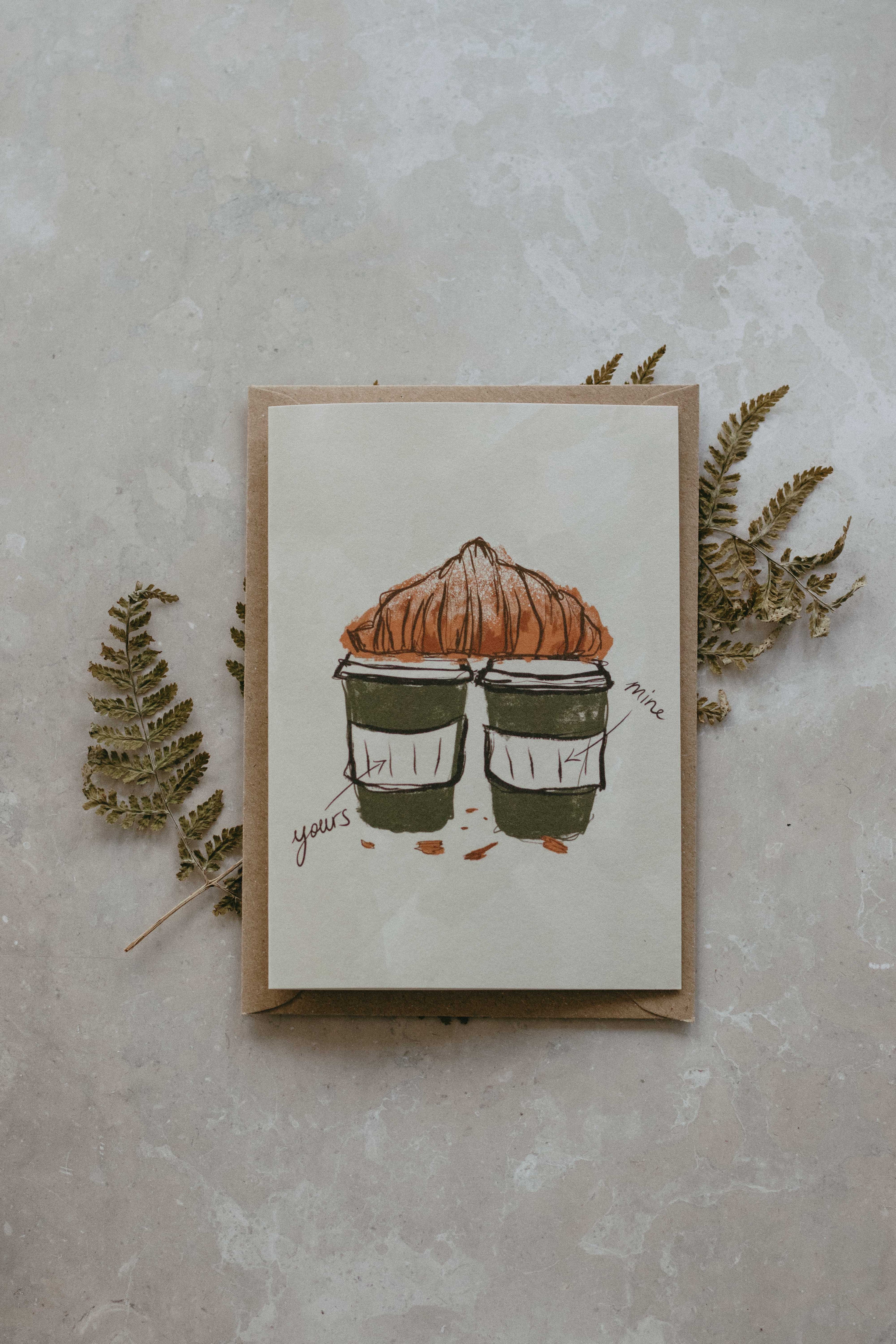 Card with illustration of two coffee cups and a pastry on a textured surface with leaves.